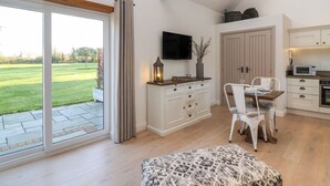 A modern kitchen with a TV, dining table, and chairs, and a large sliding glass door leading to a garden. - Church View Retreat (Weston-super-Mare)