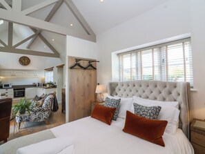 A spacious bedroom with a large bed, a wooden wardrobe, a dining area, and a kitchen. - Church View Retreat (Weston-super-Mare)