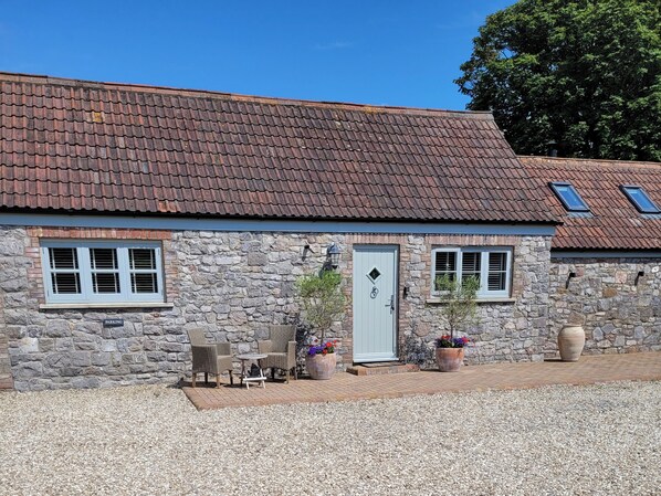 A stone building with a tiled roof, a door, and a small porch area with seating and planters. - Church View Retreat (Weston-super-Mare)
