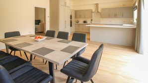 Una cucina moderna con mobili chiari in legno, un'isola centrale e un'area pranzo con tavolo in legno e sedie nere.