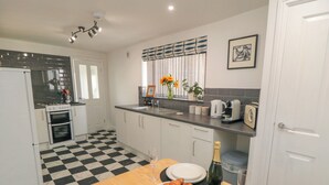 A modern kitchen with a checkered floor, white cabinets, a sink, and a dining table set with plates, a glass of wine, and a bowl of fruit. - 6 Clarence Place (Whitby)