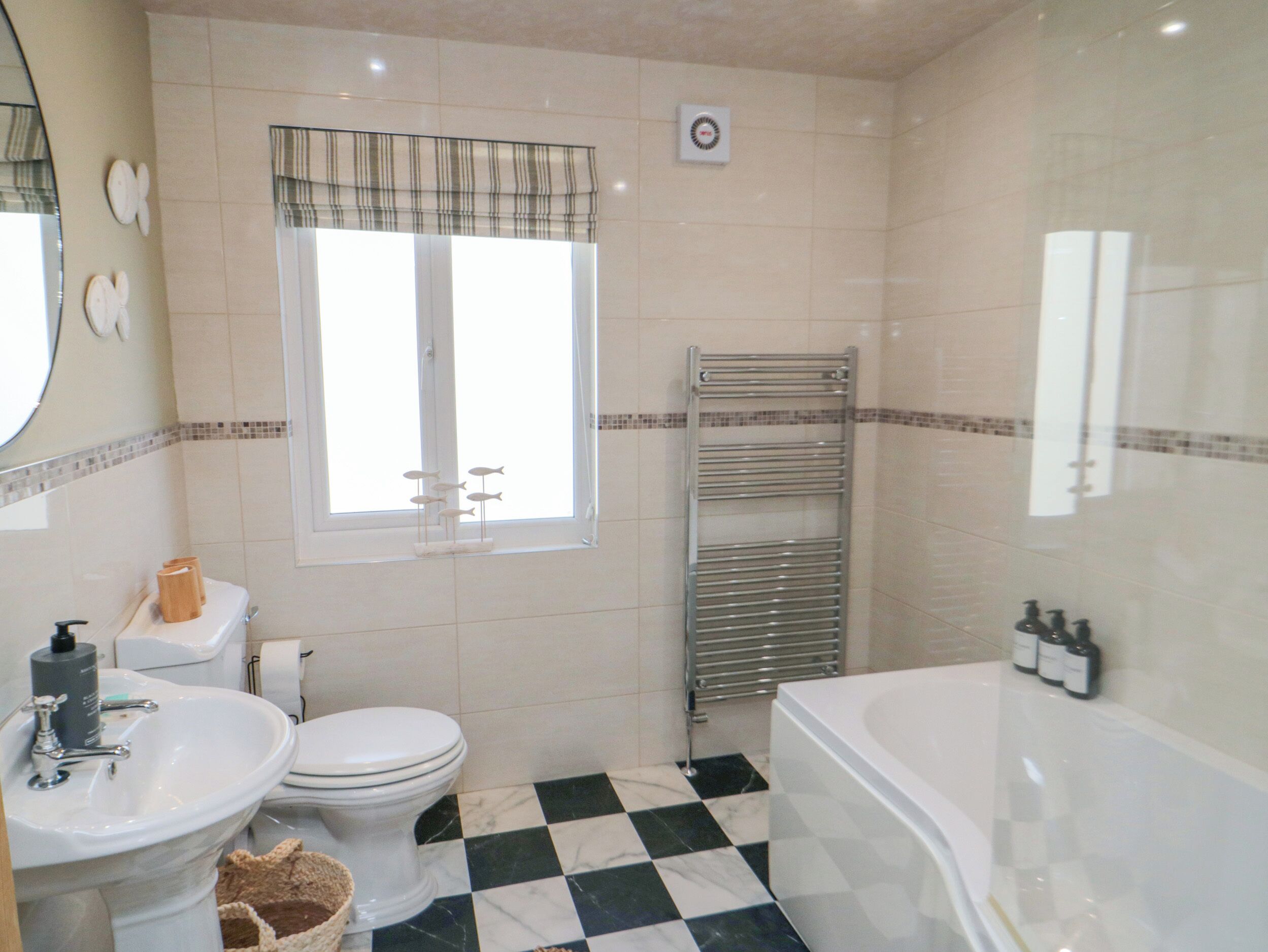Un baño con piso a cuadros, inodoro, lavamanos, bañera y ventana con cortina.