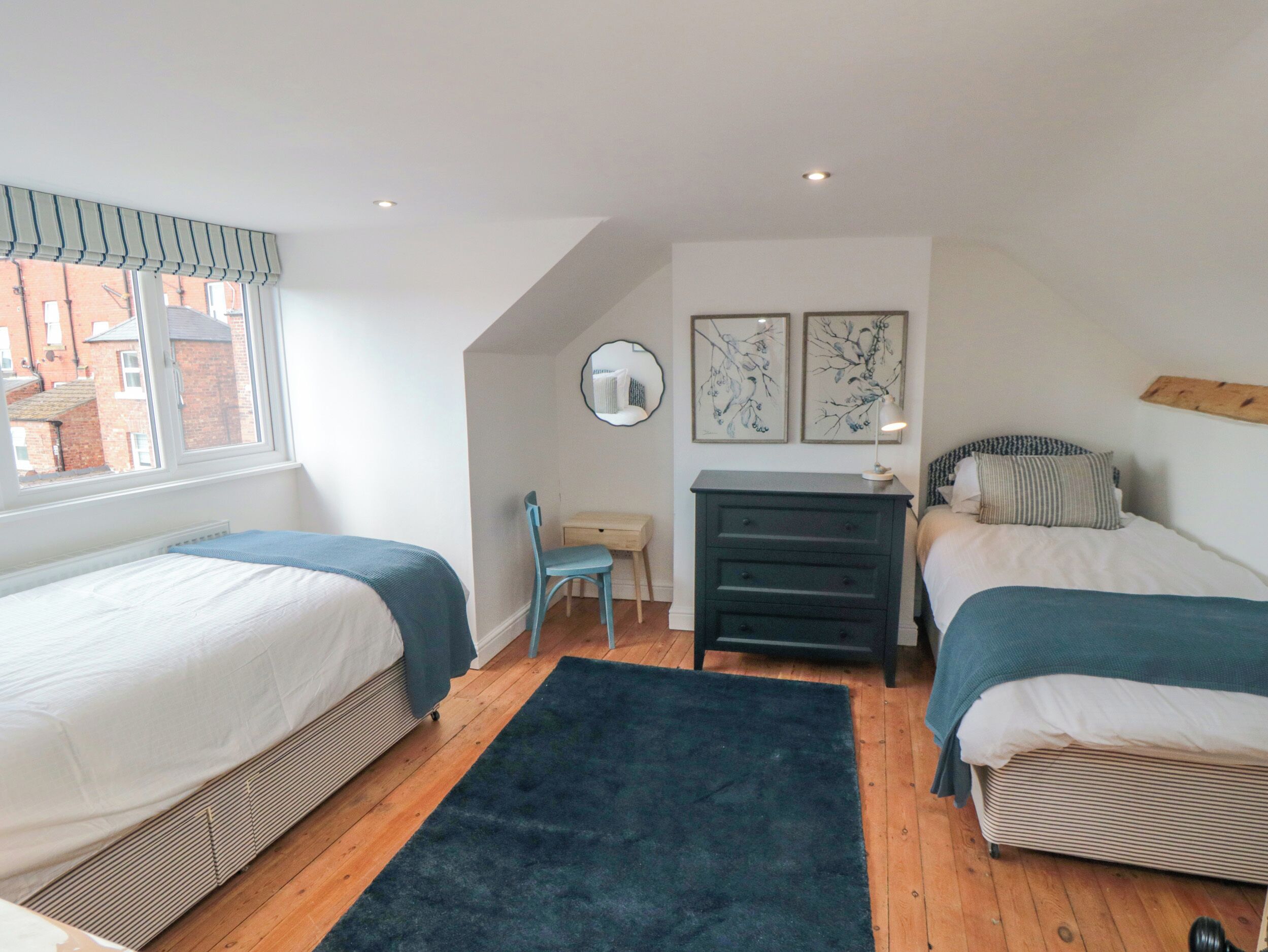 A bedroom with two beds, a desk, a chair, and artwork on the walls.