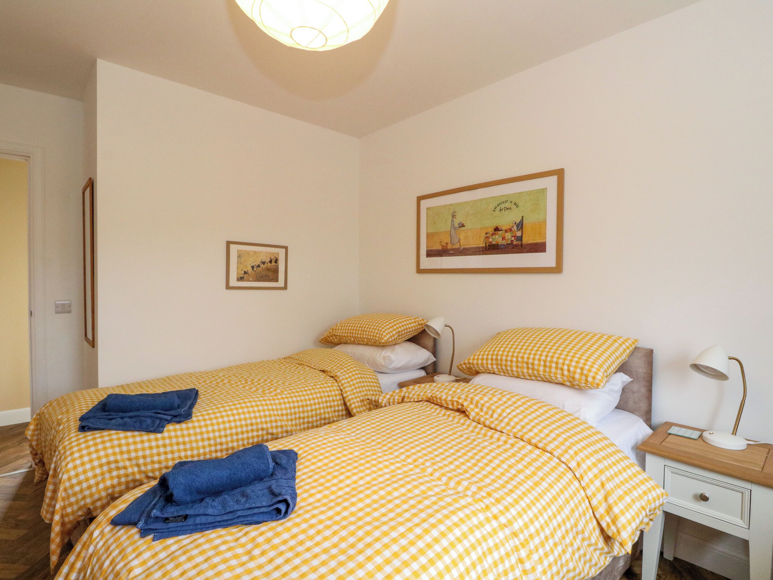 Habitación de hotel con dos camas, ropa de cama a cuadros, una mesita de noche con lámpara y un cuadro en la pared.