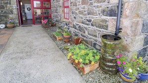 Un bâtiment en pierre avec une porte et des fenêtres rouges, un chemin de gravier et diverses plantes en pot.