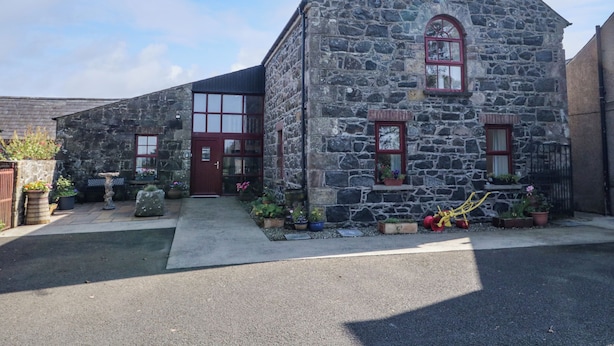 Un bâtiment en pierre avec une porte et des fenêtres rouges, entouré de plantes en pot et d’une zone pavée.