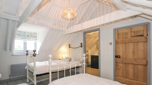 Ein Schlafzimmer mit schrägem Dach, einer Holztür, einem weißen Bett und einer kleinen Bank.