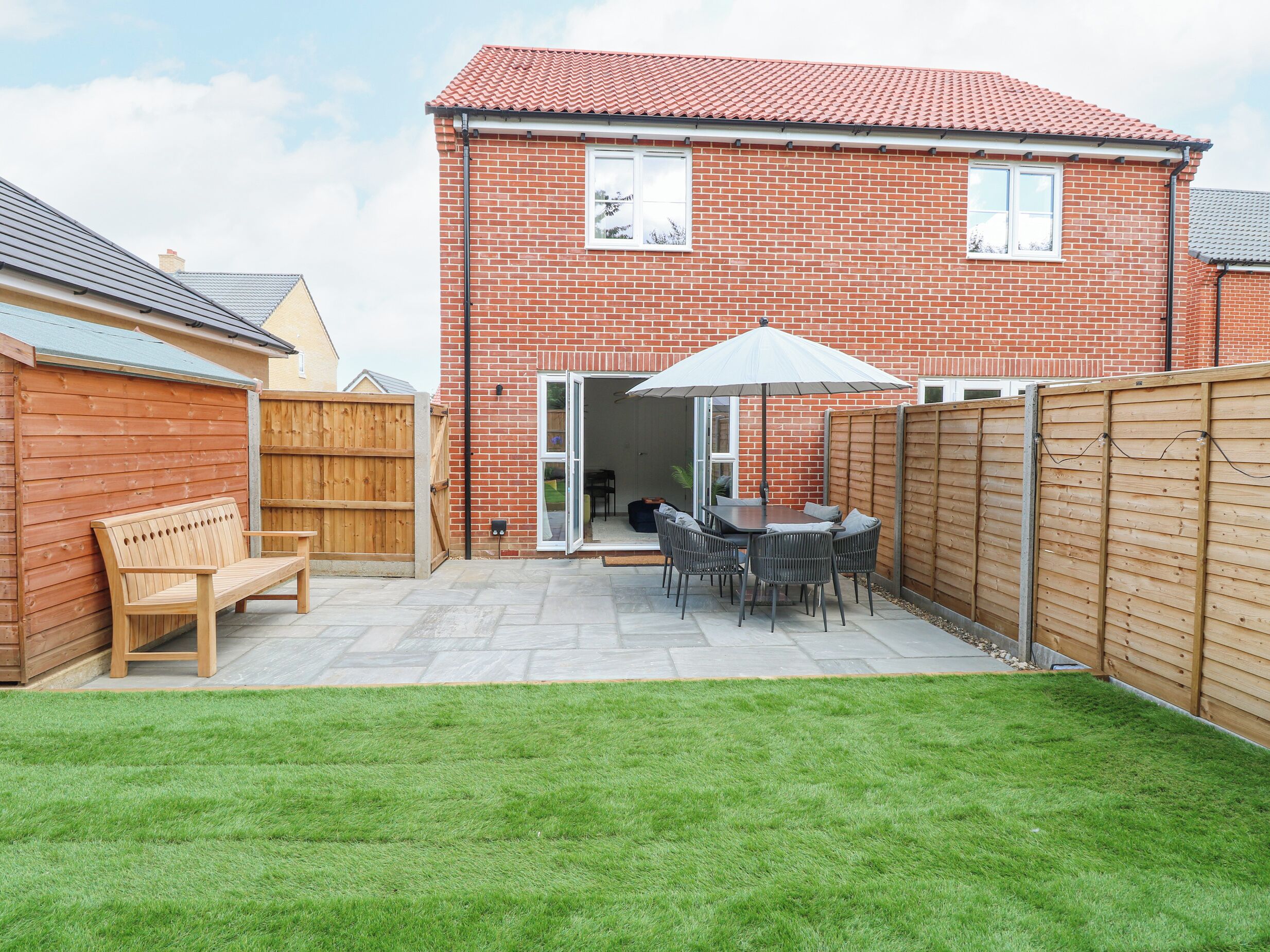 A brick house with a patio, a wooden fence, and a bench.