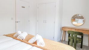 Une chambre d’hôtel avec un lit, un bureau en bois, une chaise verte et un miroir au mur.