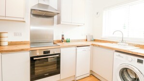 Une cuisine moderne avec des armoires blanches, une hotte de cuisinière en acier inoxydable, un four, un lave-vaisselle et un lave-linge encastré.