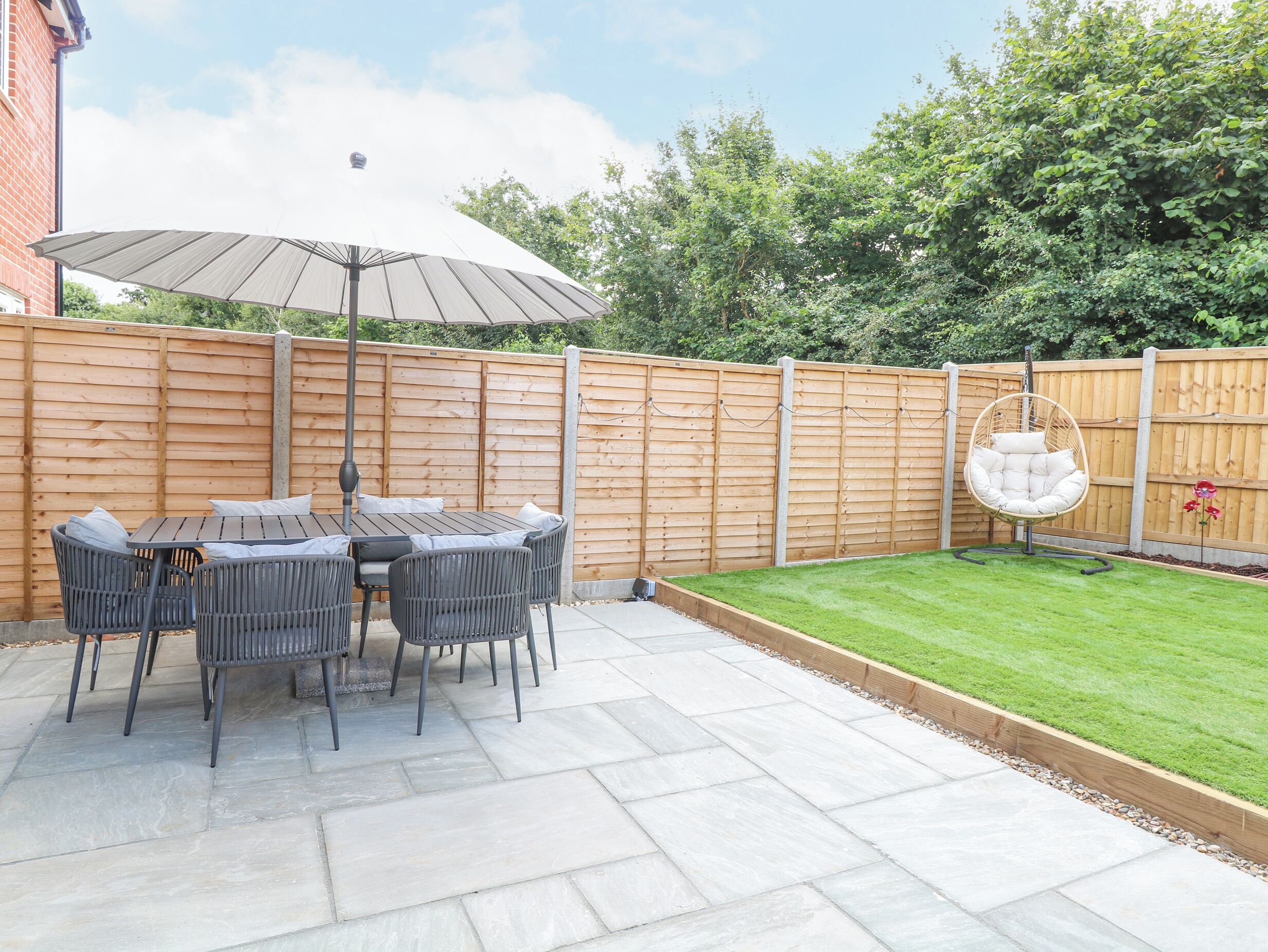 A patio with a table and chairs, a hanging chair, and a wooden fence.