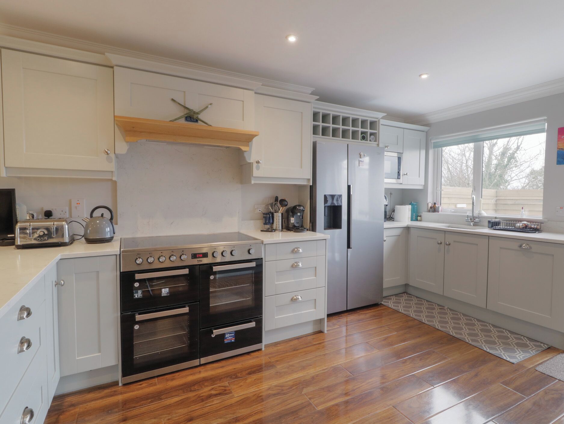 A modern kitchen with white cabinetry, a stainless steel refrigerator, a built-in oven, and a wooden countertop.
