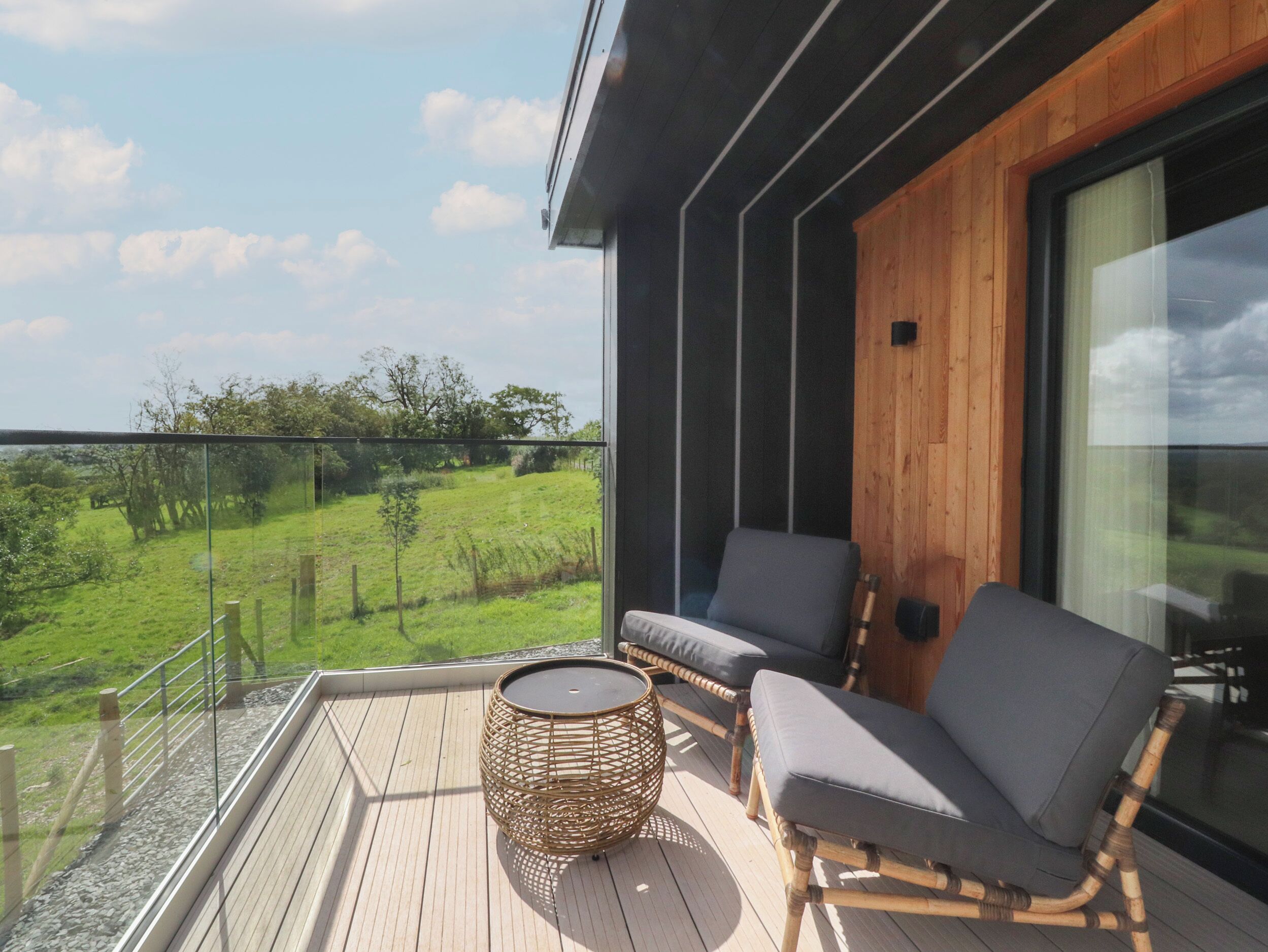 A balcony with two wicker chairs and a small table, overlooking a green landscape.