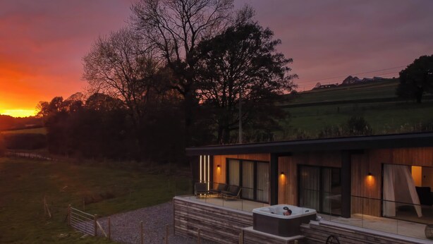 A modern house with a hot tub on the porch, surrounded by a fence and a grassy field. - The Lookout (Preston)