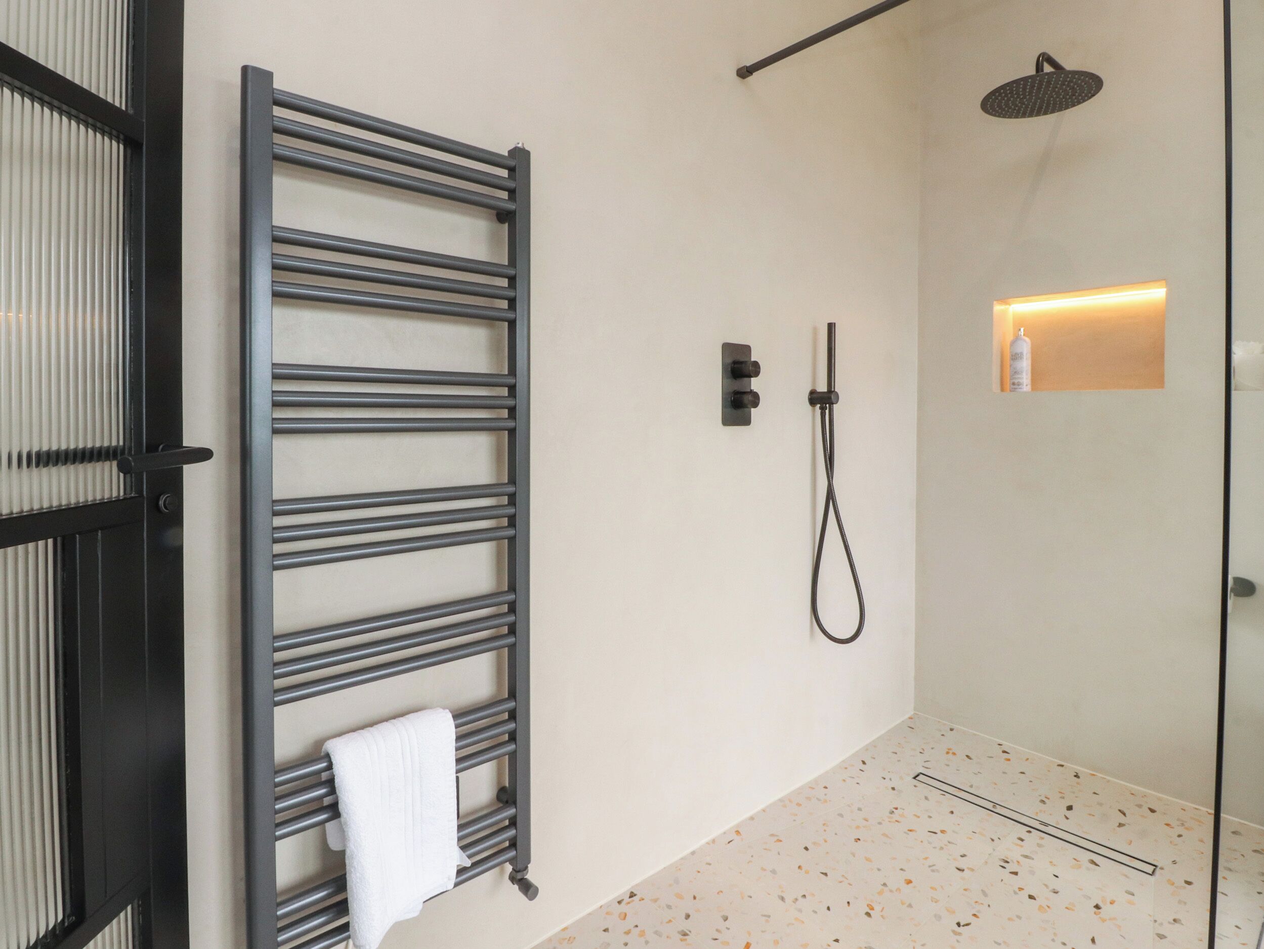 Un baño moderno con cabina de ducha de vidrio, un perchero y una lámpara de pared.