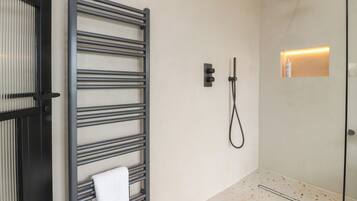 Un baño moderno con cabina de ducha de vidrio, un perchero y una lámpara de pared.
