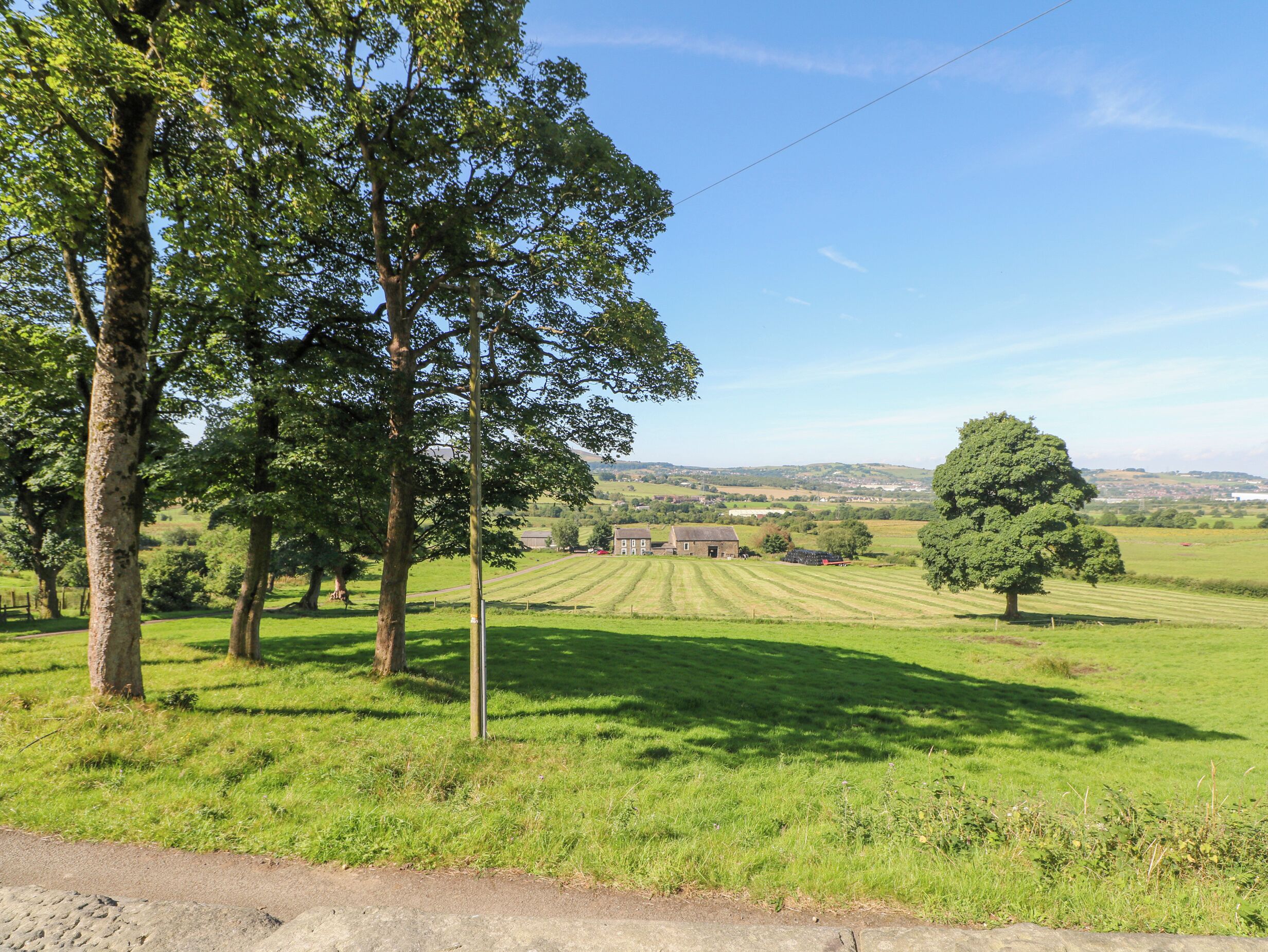A rural landscape with a large field, a few trees, and a distant building.