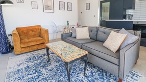 A modern living room with a sofa, armchair, and coffee table, a kitchen area with dark cabinets, and a dining table with chairs. - Priestleys Retreat (Blackburn)