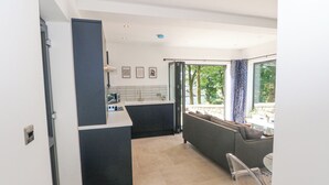 A modern kitchen with a central island, a dining area with a sofa, and a large sliding glass door leading to a balcony. - Priestleys Retreat (Blackburn)