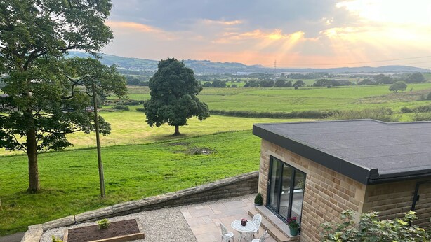 A patio area with a table and chairs, surrounded by potted plants and a view of a green field and distant hills. - Priestleys Retreat (Blackburn)