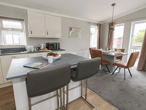 Et moderne køkken med spiseplads, der inkluderer en central ø med barstole, en mikrobølgeovn og en skål med frugt.