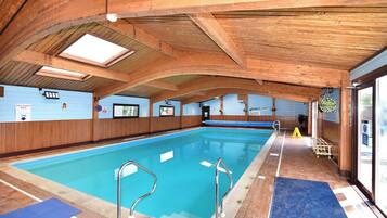 An indoor swimming pool with wooden beams, clear signage, and a blue mat at the pool's edge.
