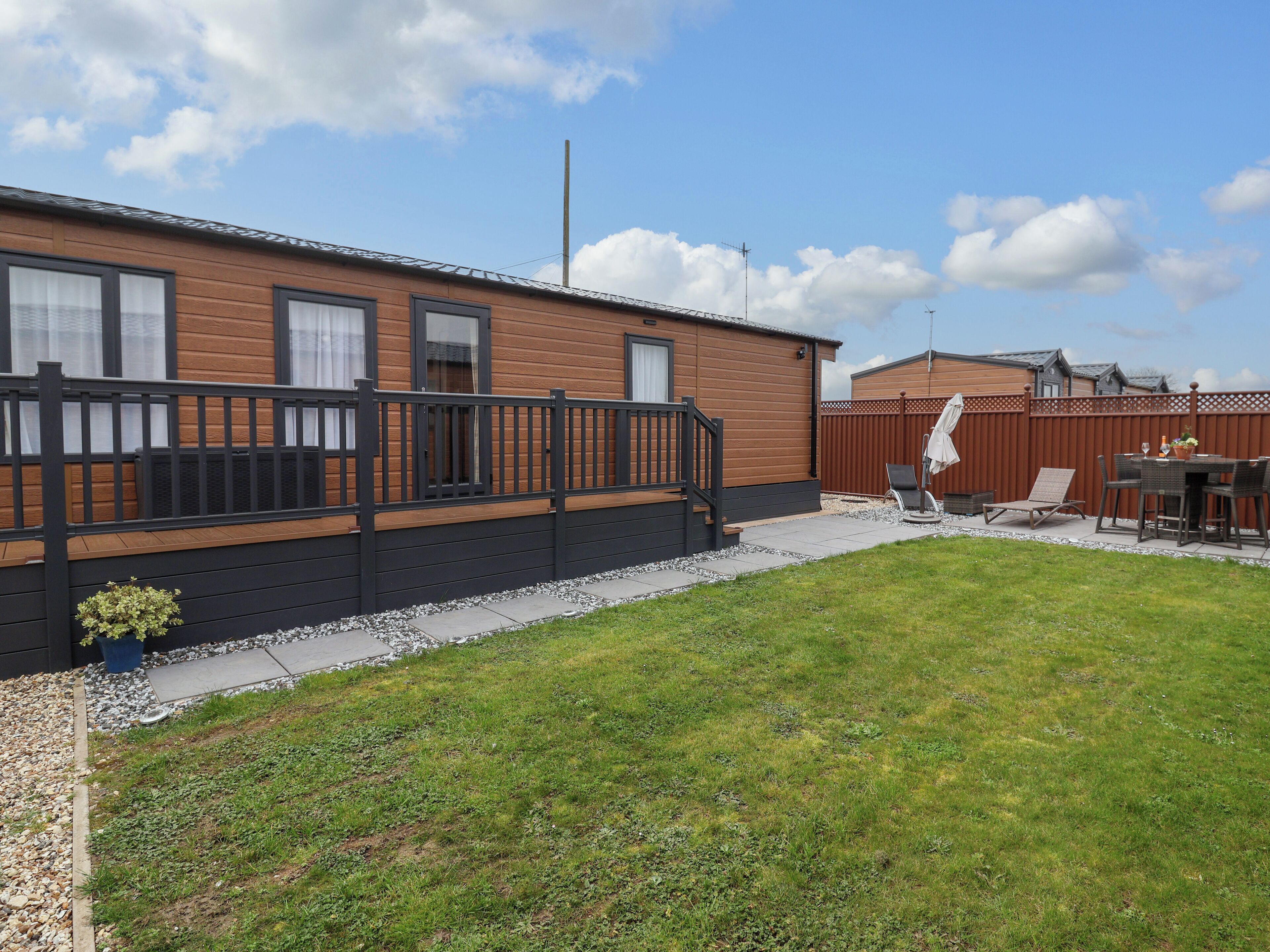 En mobilhome med terrasse, en lukket baghave og en patio med udendørs møbler.