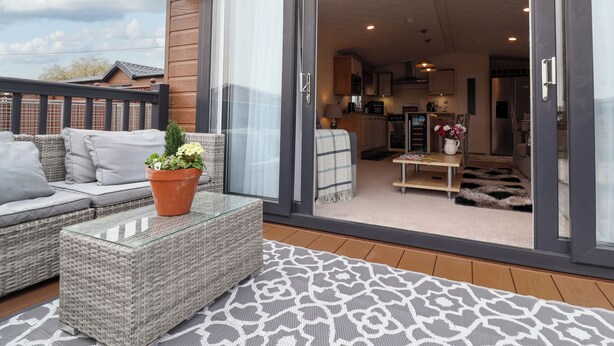 Eine moderne Terrasse mit Korbmöbeln, einem Glastisch und einem Blumentopf.
