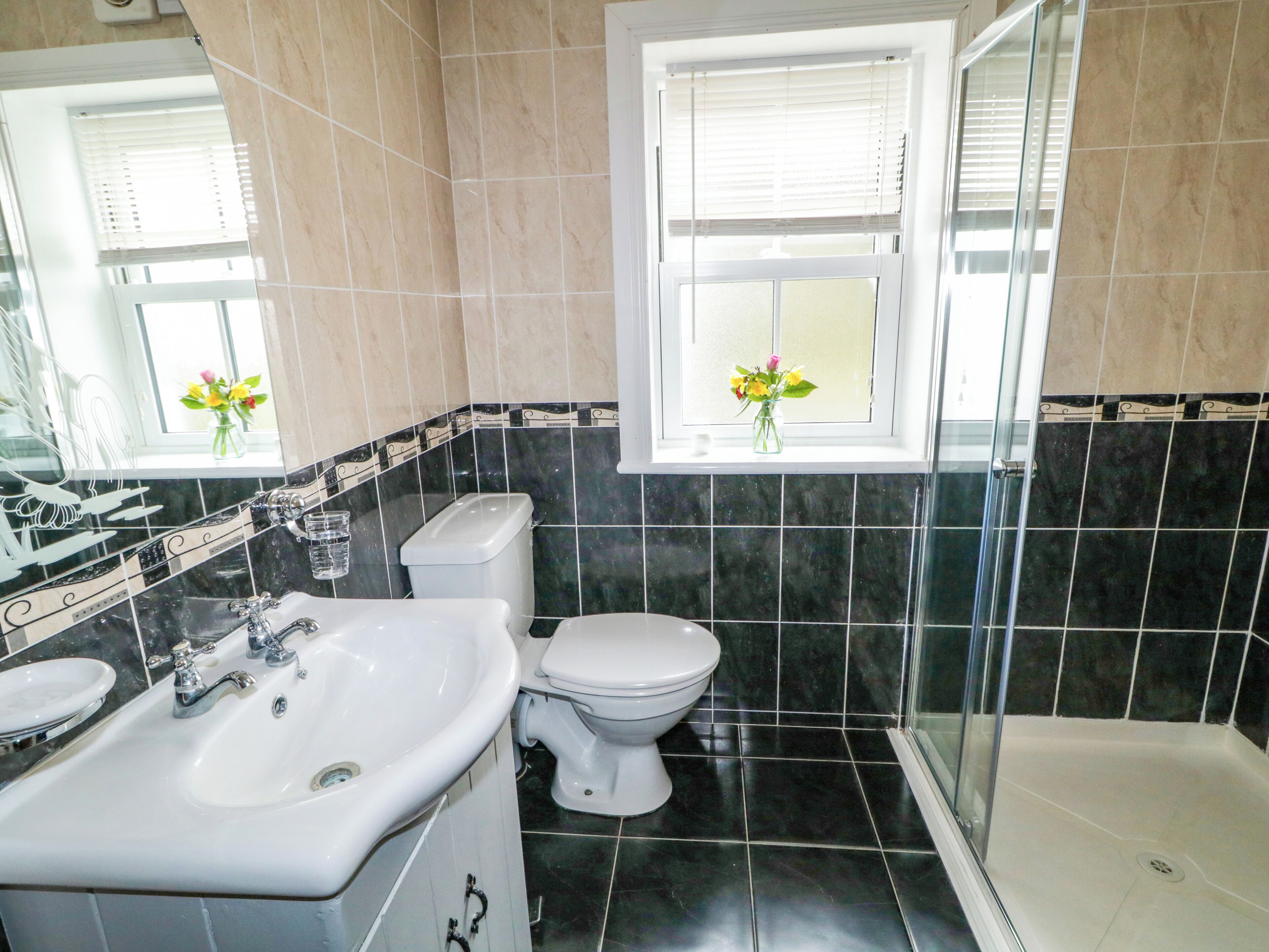A bathroom with a sink, toilet, and shower. There is a window with a view of the outside.