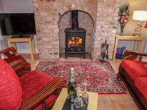 A cozy living room with a brick fireplace, a television, and red furniture. - Ballard Cottage (Newry)