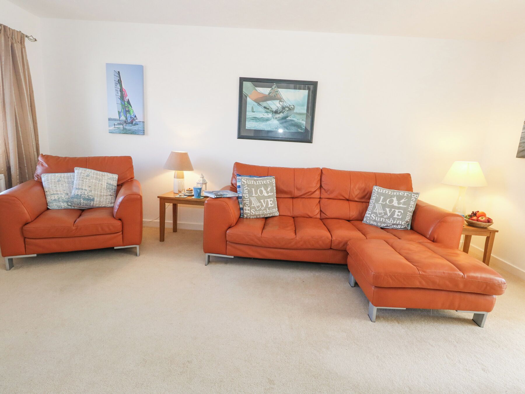 A living room with two orange sofas, a small table with a lamp, and two wall-mounted pictures.