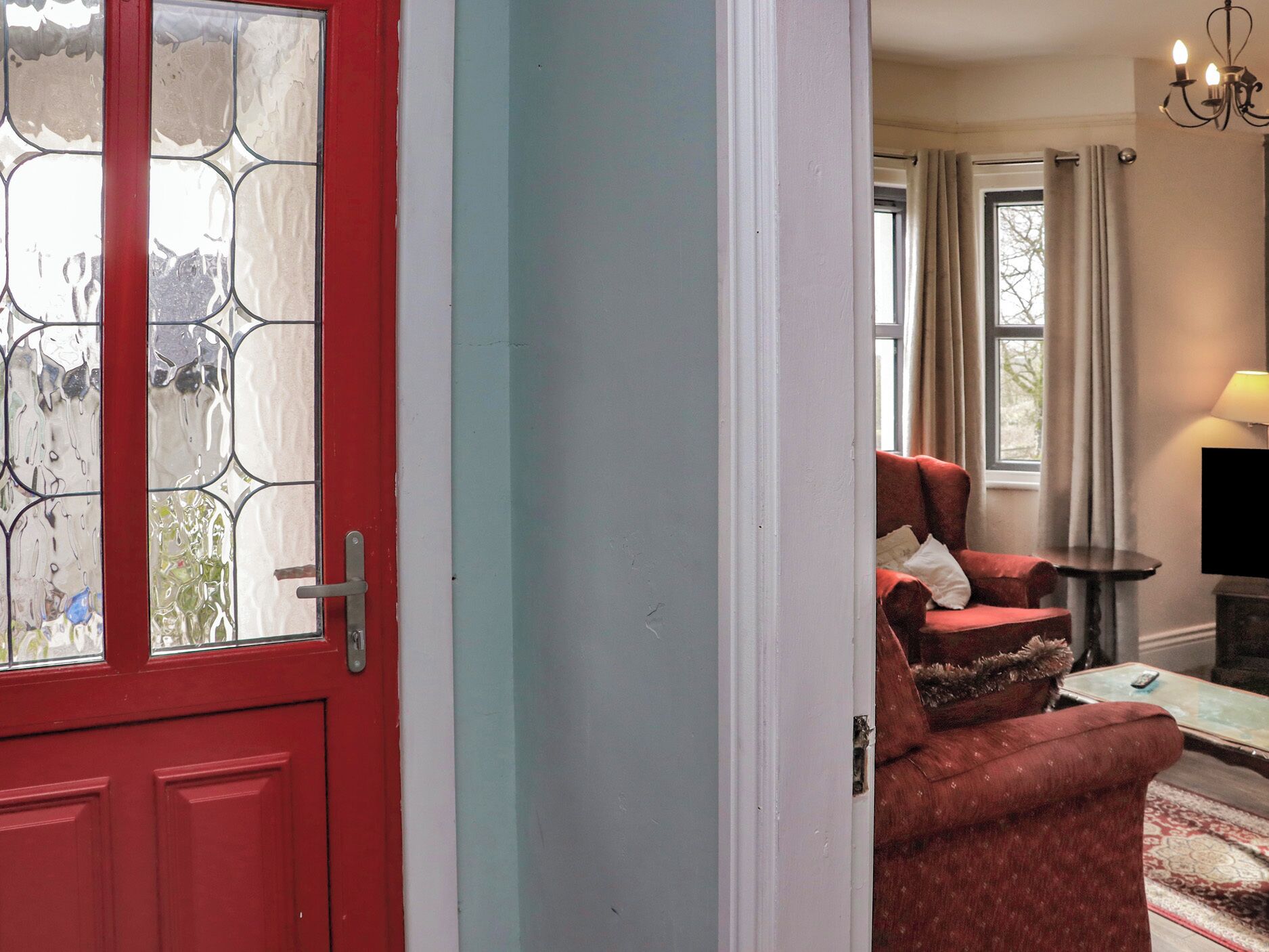 Una puerta roja con un panel de vidrio, un sillón rojo, una mesita y una lámpara.
