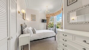 A bedroom with a bed, bedside table, dresser, and a television. - Fir Trees (Windermere)