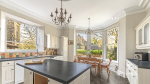 A spacious kitchen with a large island, white cabinetry, and a view of the garden through large windows. - Fir Trees (Windermere)