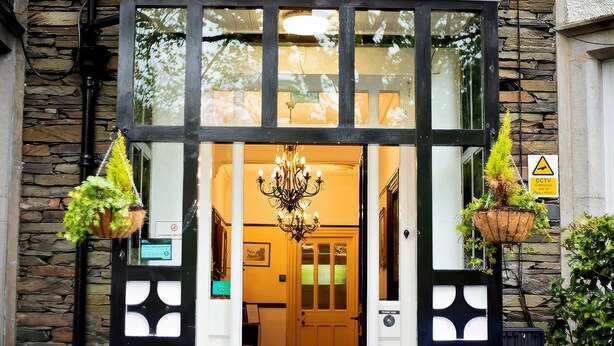 A hotel entrance with a stone facade, black-framed glass doors, and hanging planters. - Fir Trees (Windermere)