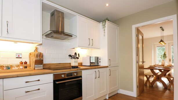 Una cocina moderna con armarios blancos, una campana extractora de acero inoxidable y una encimera de madera.