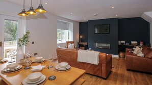 Una sala de estar moderna con una mesa de comedor de madera dispuesta para cuatro personas, un sofá de cuero marrón y un televisor montado en la pared.