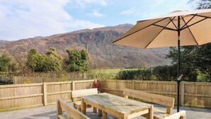 Un patio al aire libre con muebles de madera y un gran paraguas, con vistas a un paisaje montañoso.