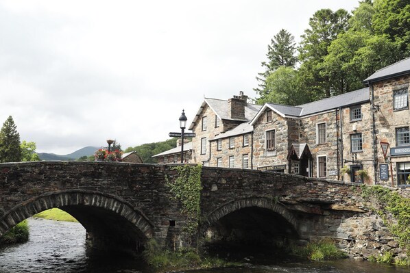 A stone bridge over a river with buildings on either side, including a pub named "Robinsons". - Craig y Llan (Caernarfon)