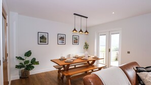 Un comedor con una mesa de madera, bancos y lámparas colgantes. Hay cuadros en la pared y una planta en maceta en el suelo.