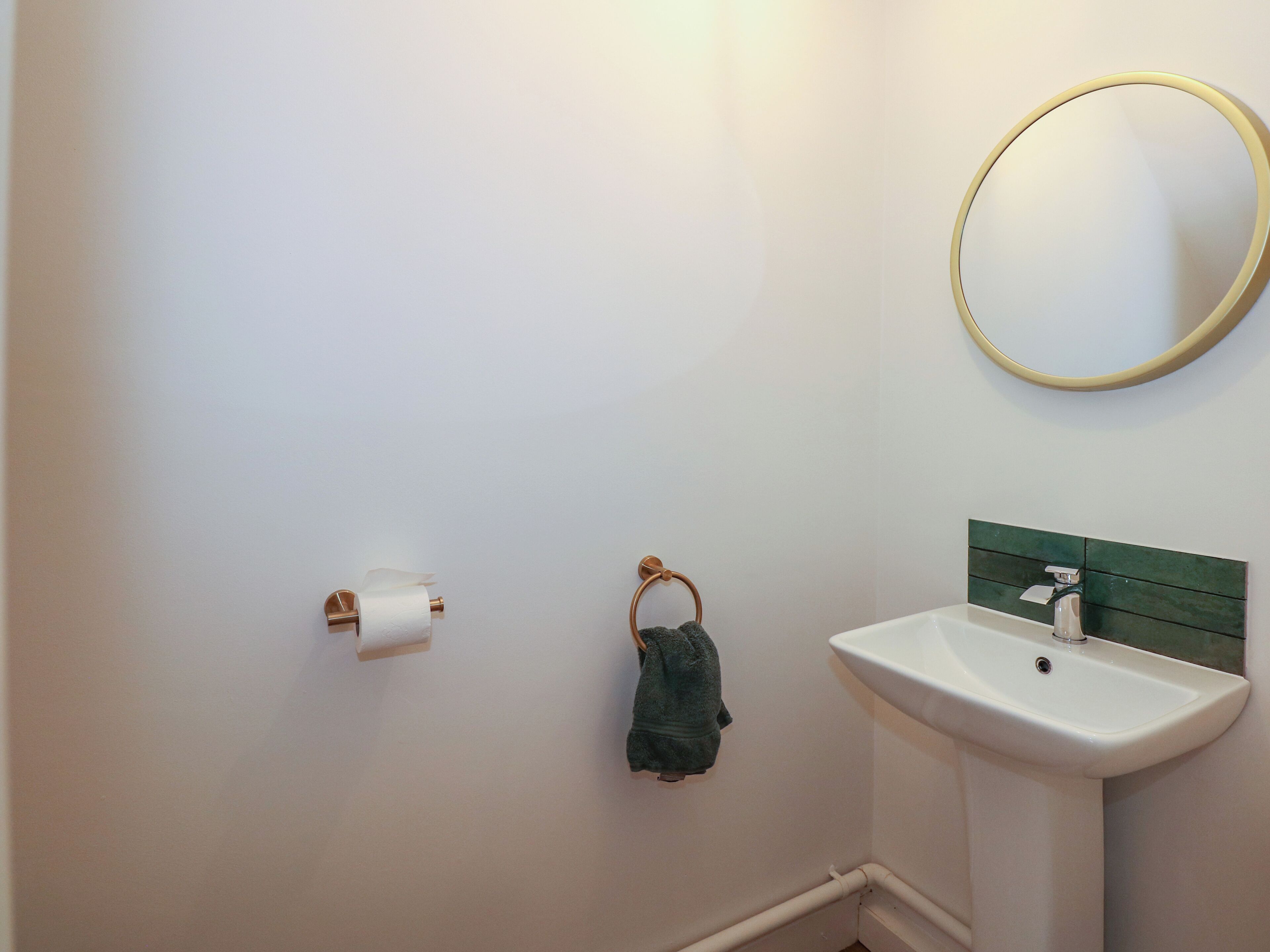 A bathroom with a white sink, a green towel ring, and a toilet paper holder.
