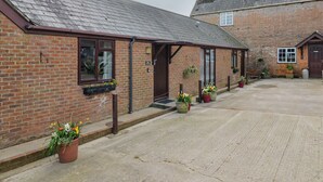 A brick building with a sloped roof, a front door, and potted plants. - Daisy Cottage (Bridport)