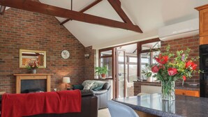 A living room with a fireplace, a sofa, a coffee table, and a kitchen area with a countertop and a potted plant. - Daisy Cottage (Bridport)