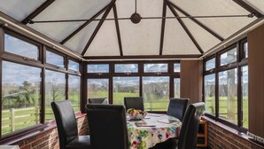 A conservatory with a table and chairs, large windows, and a view of the outdoors. - Daisy Cottage (Bridport)