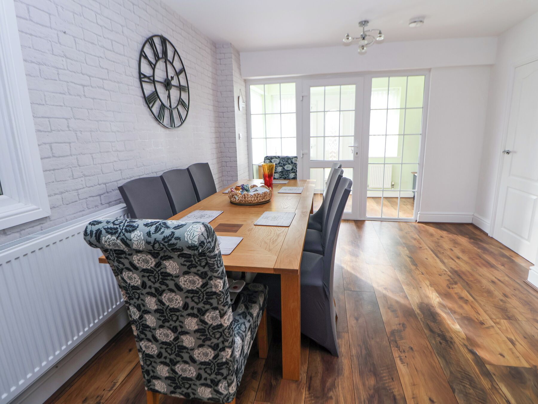 Un comedor con una mesa de madera, sillas estampadas y un reloj de pared.