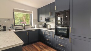 A modern kitchen with dark cabinetry, a built-in oven, and a window with a view of greenery. - Hogans Cottage (Ennistimon)