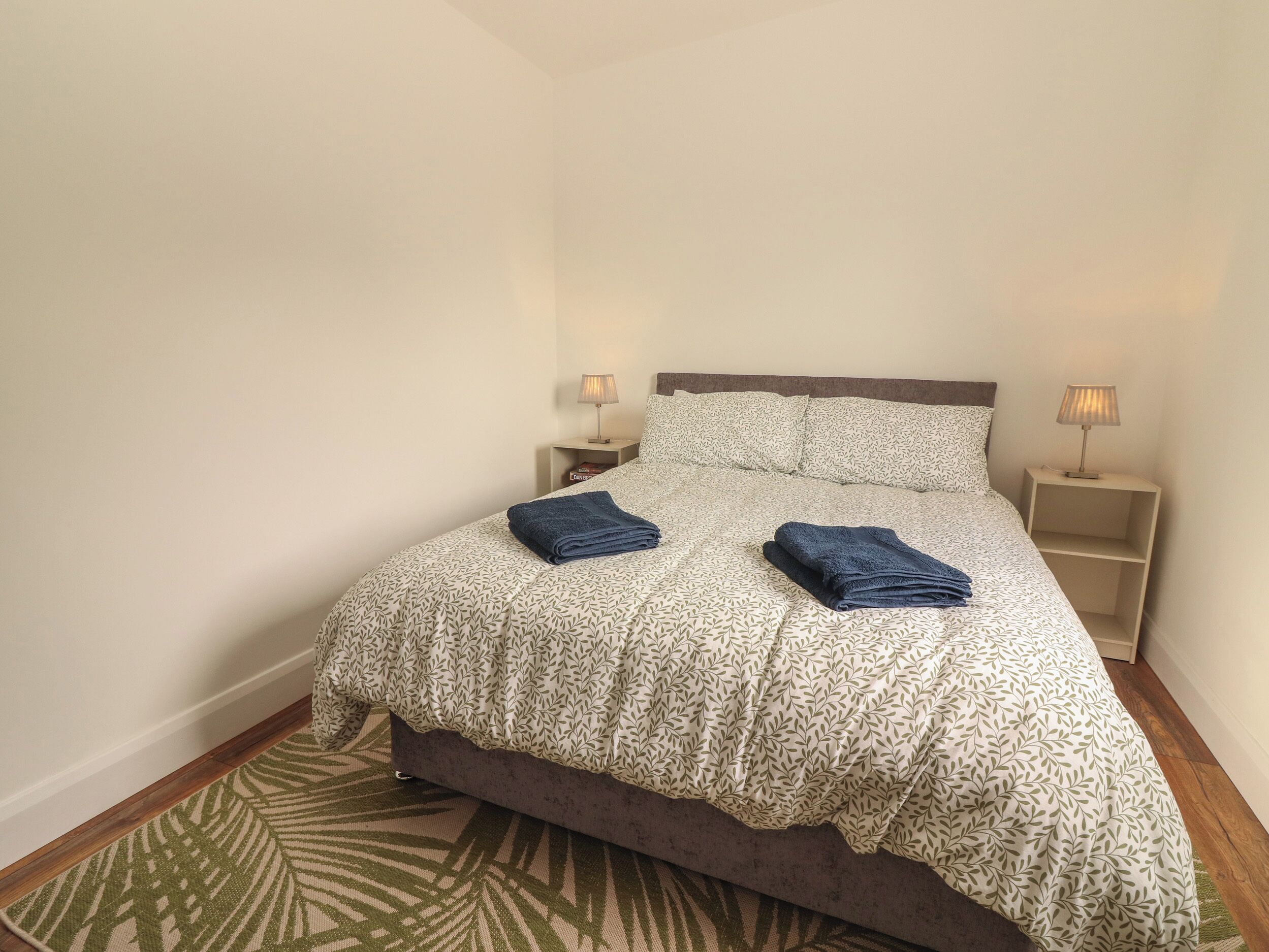 A neatly made bed with patterned bedding, two bedside lamps, and a small bedside table.