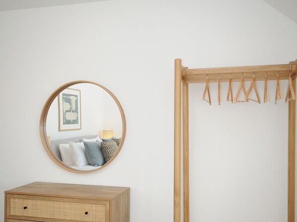 Une chambre avec un miroir rond, une armoire en bois et un étendoir à linge en bois.