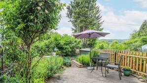 Une terrasse avec une table et des chaises, entourée d’une végétation luxuriante et d’une clôture en bois.