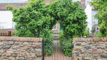 Enter a charming village through this traditional stone gate, surrounded by lush gardens and quaint brick buildings.